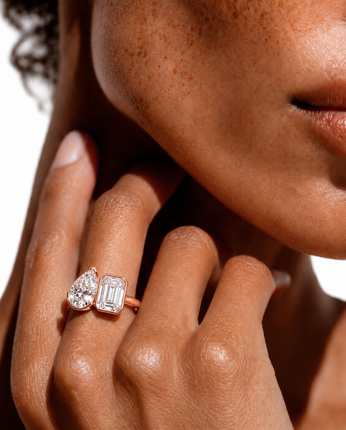 color_10K_RG, color_14K_RG &&A close-up lifestyle shot of a model's hand wearing a rose gold ring with a pear-cut diamond and an emerald-cut diamond, set against a clean white background.