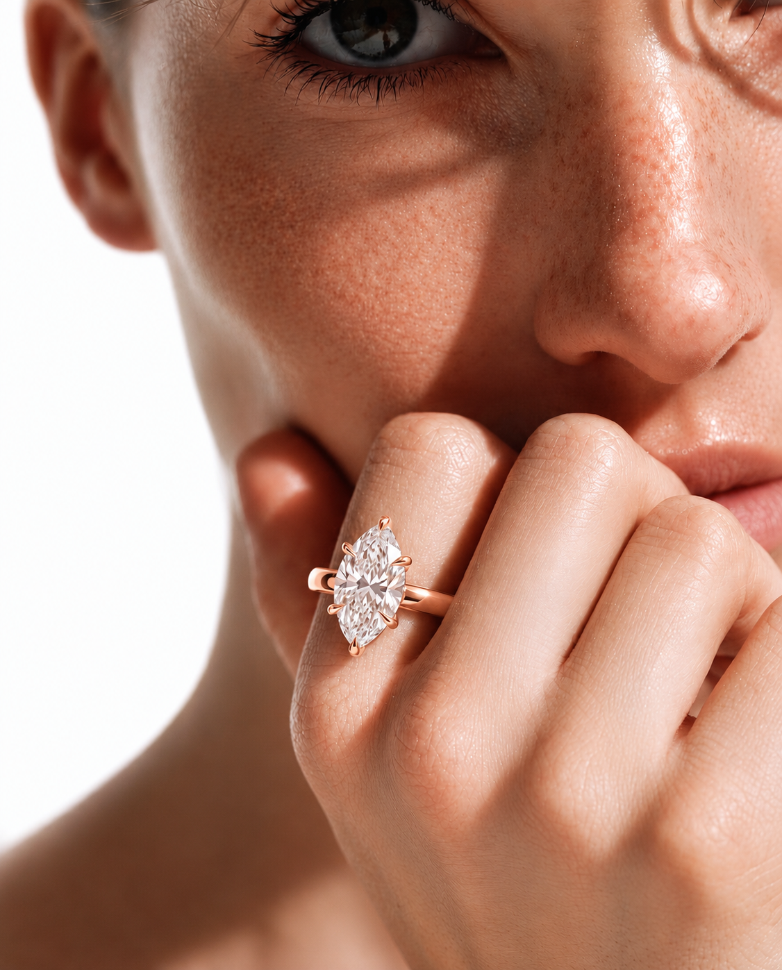color_10K_RG, color_14K_RG &&A close-up lifestyle shot of a model wearing a rose gold ring with a marquise-cut diamond. The ring is shown on the model's finger, with dramatic, high-contrast sunlight casting shadows across her face and hand.