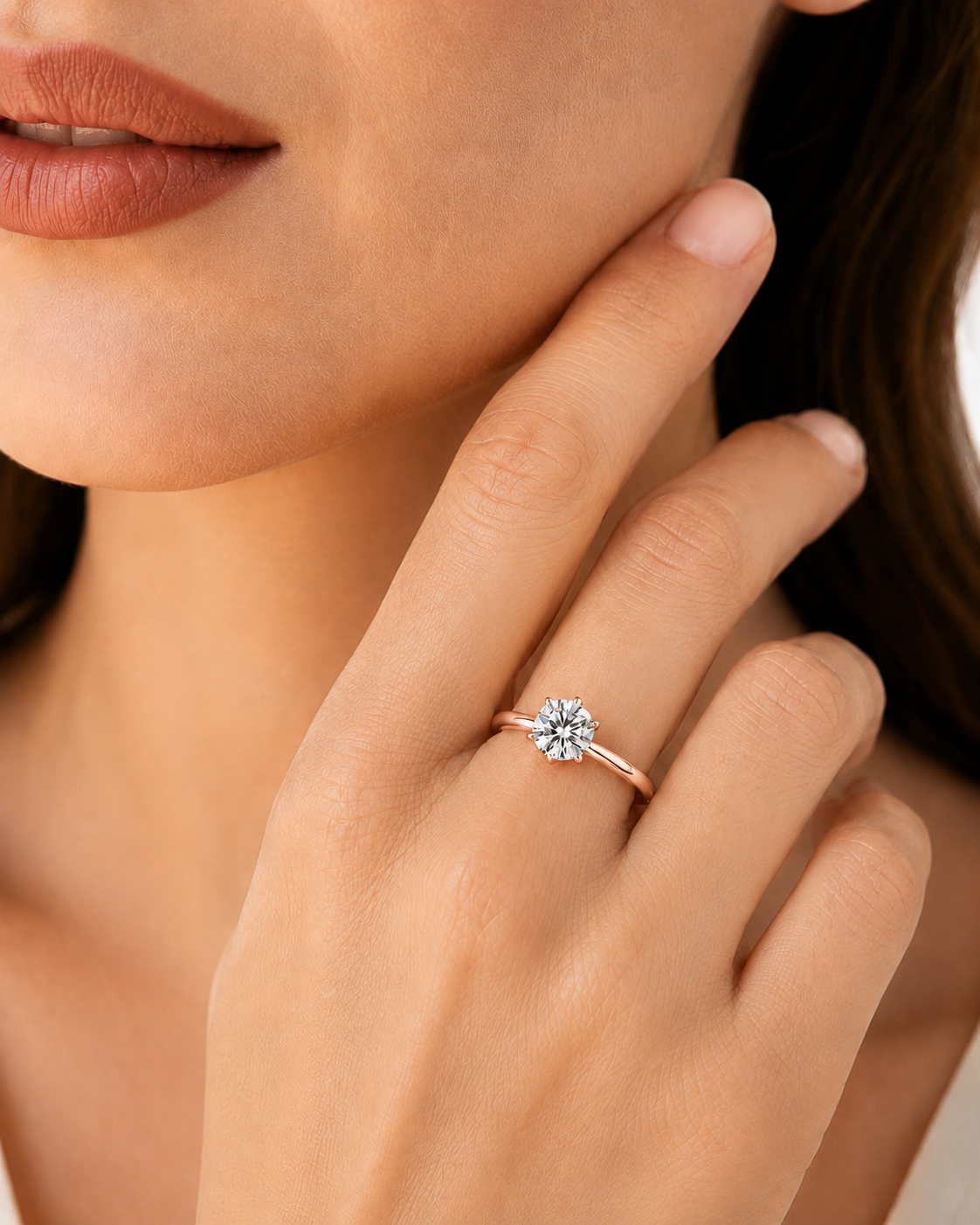color_10K_RG, color_14K_RG &&A close-up lifestyle shot of a woman wearing a rose gold ring with a round-cut clear gemstone on her finger.