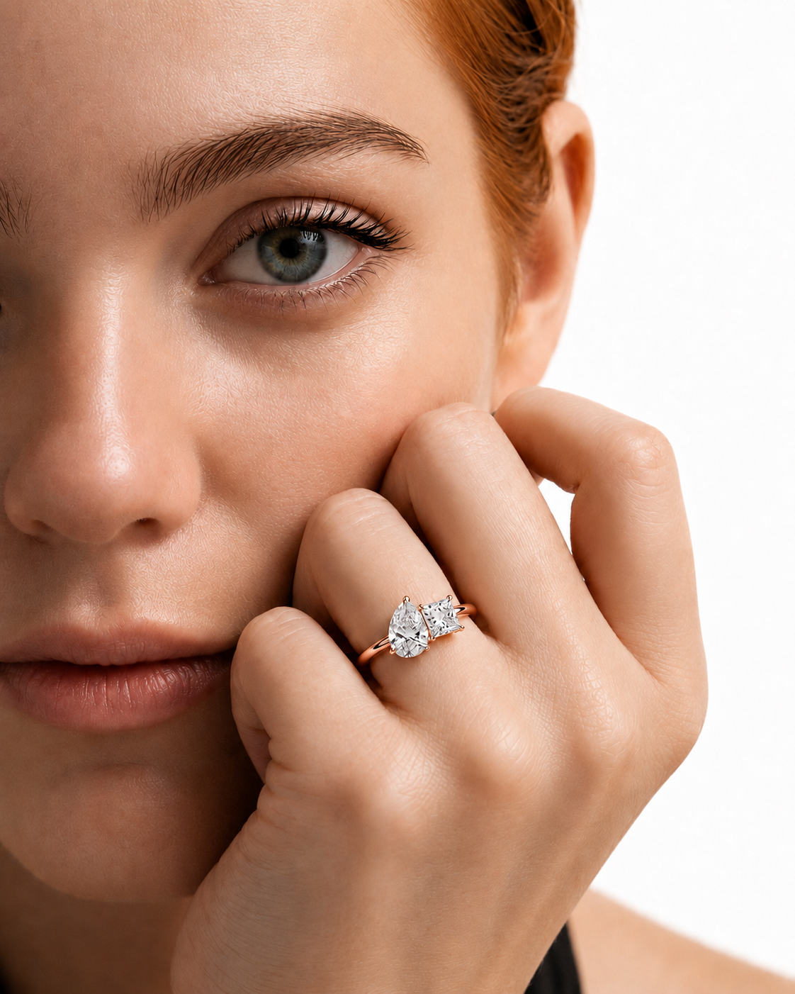 color_10K_RG, color_14K_RG && close-up lifestyle shot of a woman with red hair wearing a rose gold ring with a pear-cut diamond. Her hand is resting against her cheek, and the background is a clean white studio backdrop.