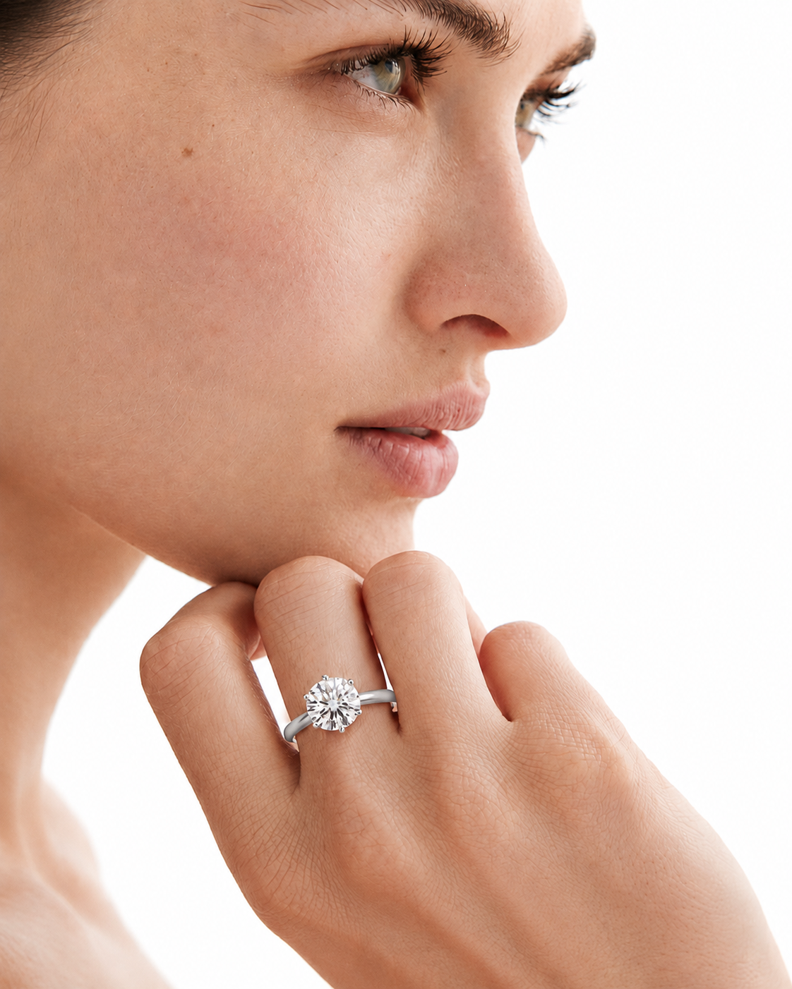 color_925_SIL,color_935_ARG,color_10K_WG, color_14K_WG &&A close-up profile of a woman with her hand resting near her chin, wearing a silver-toned diamond engagement ring on her ring finger against a clean white background.