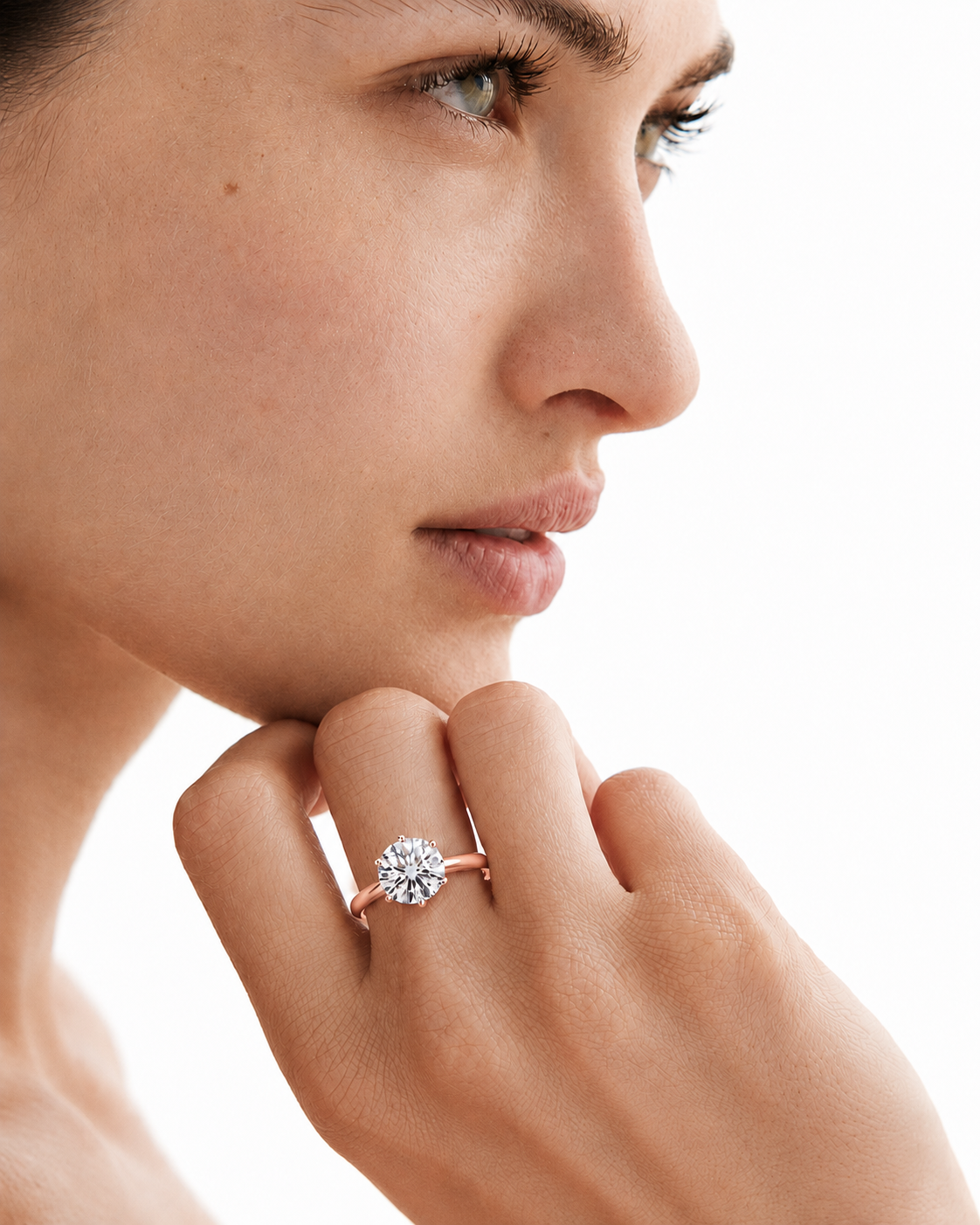 color_10K_RG, color_14K_RG &&A close-up lifestyle shot of a woman wearing a rose gold ring with a round-cut clear gemstone on her finger, set against a clean white background.
