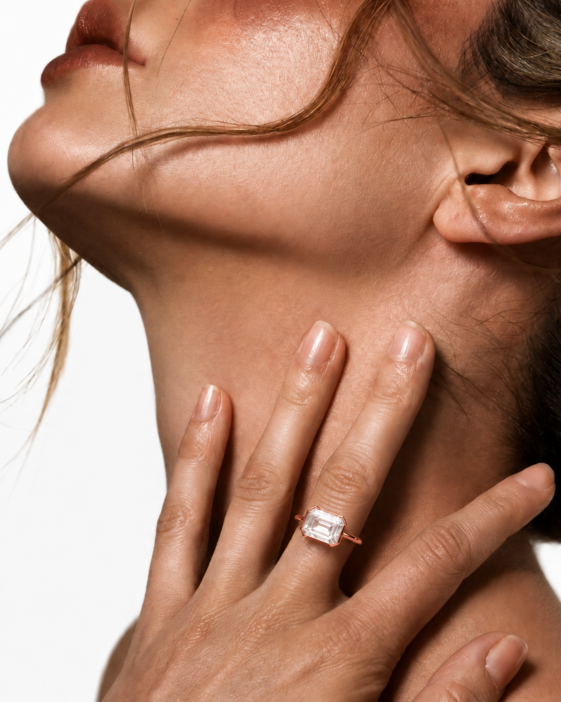 color_10K_RG, color_14K_RG &&A close-up lifestyle shot of a model wearing a gold ring with a rectangular emerald-cut clear gemstone on her finger, set against a clean white background.