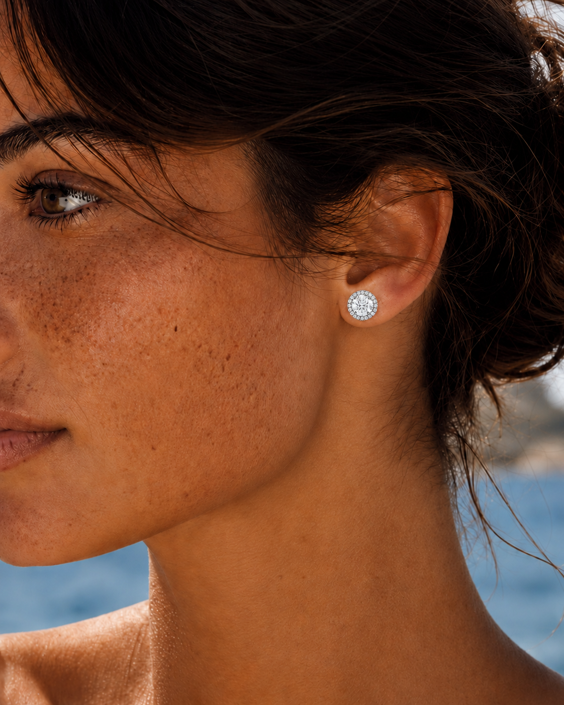 color_925_SIL,color_935_ARG,color_10K_WG, color_14K_WG &&A close-up side profile of a woman wearing a small round silver stud earring with a clear gemstone, set against a blurred outdoor background.