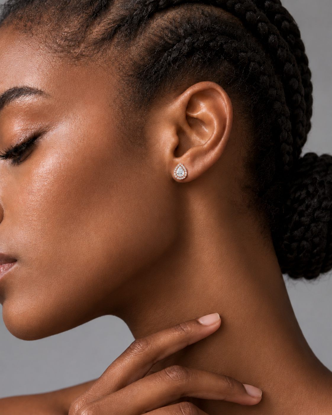 color_10K_RG, color_14K_RG &&A close-up side profile of a woman with braided hair wearing a small teardrop-shaped silver stud earring with a clear gemstone, set against a neutral gray background.