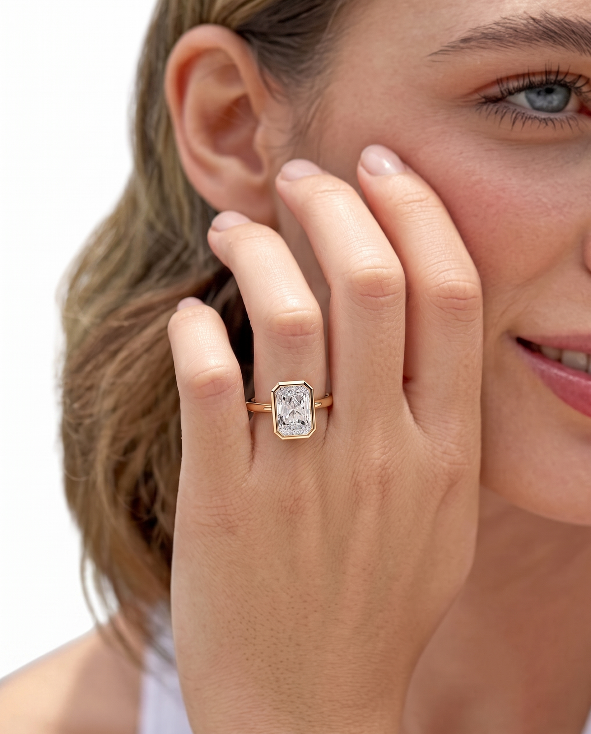 color_10K_YG, color_14K_YG &&A close-up lifestyle shot of a woman wearing a rose gold ring with a rectangular bezel-set clear gemstone on her finger, against a clean white background.