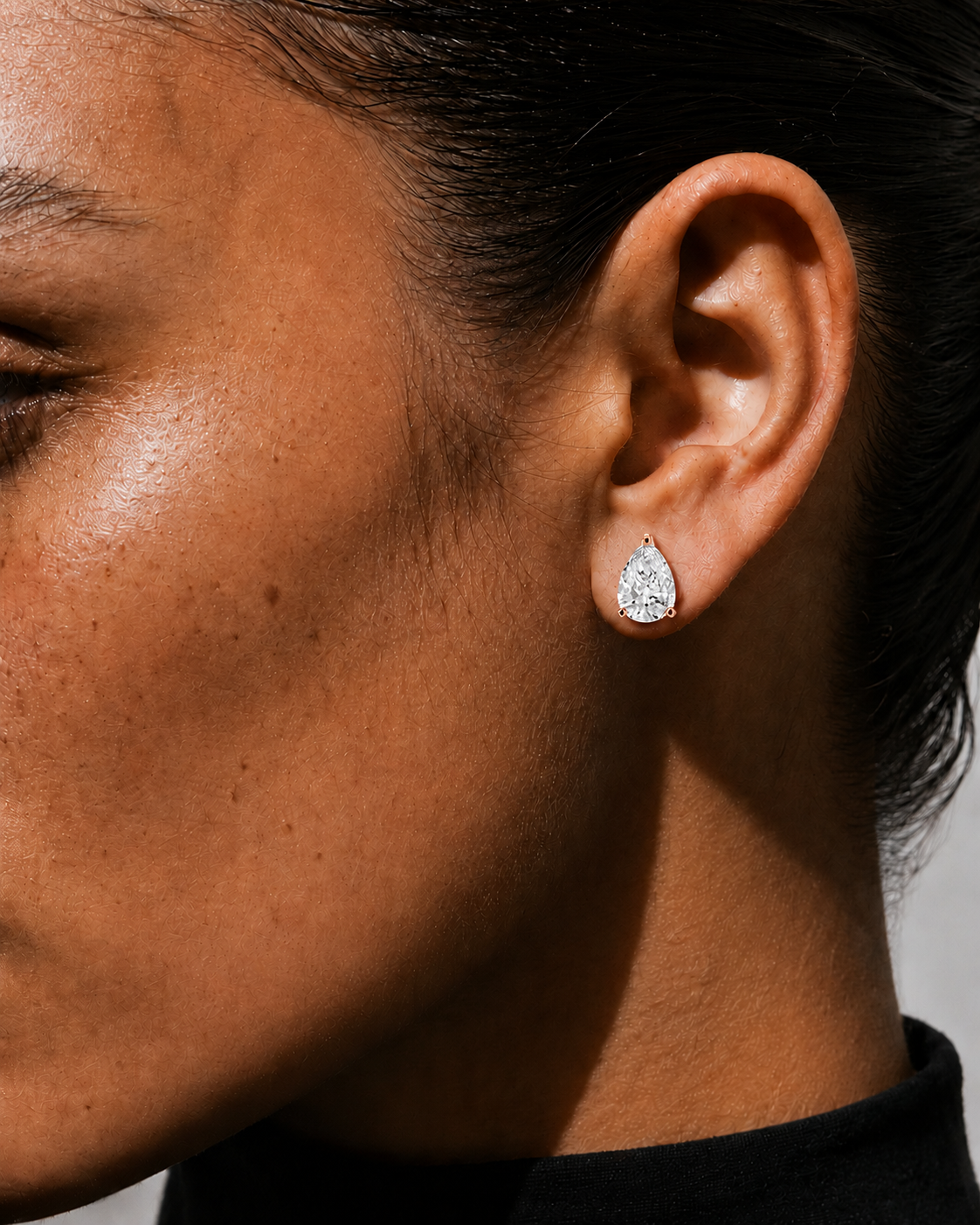 color_10K_RG, color_14K_RG &&A close-up side profile of a model wearing a small pear-cut diamond stud earring in a silver-toned setting.